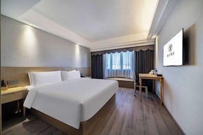 Habitación de hotel con una cama grande, una mesita de noche, un escritorio y una ventana con cortinas.