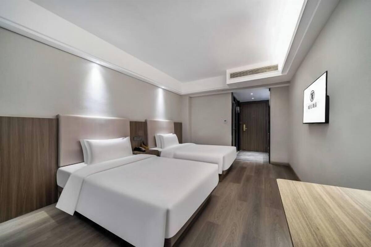 A hotel room with two beds, a wooden headboard, a small table, and a framed picture on the wall.