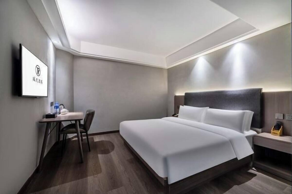 A modern hotel room with a large bed, a desk with a chair, and a nightstand.