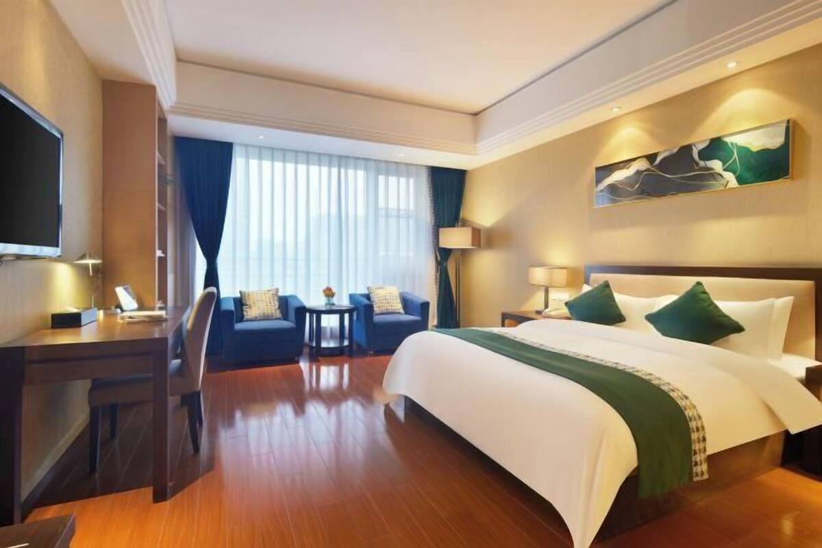 A hotel room with a bed, a desk, a chair, a TV, and a window with curtains.