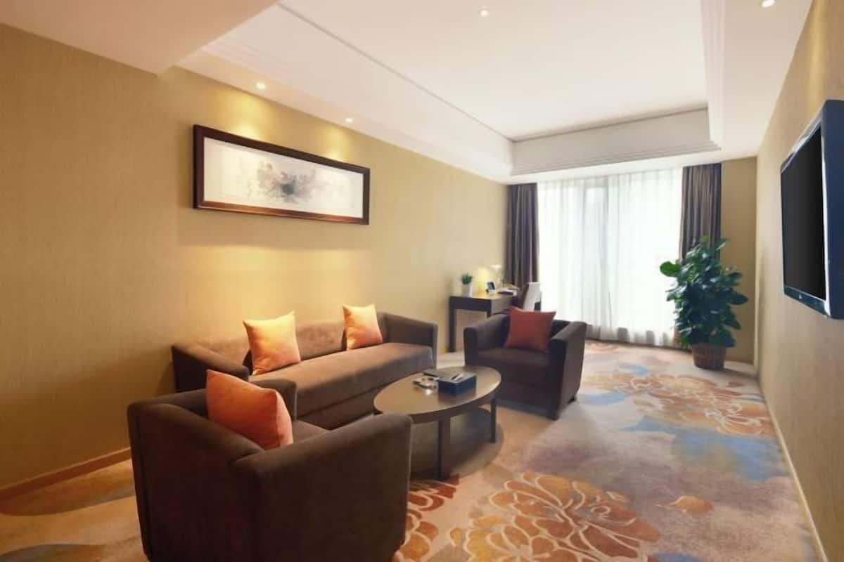 A hotel room with a sofa set, a coffee table, a TV, and a large window with curtains.