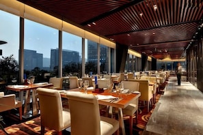 A restaurant with tables and chairs arranged for dining, large windows offering a view of the city, and a modern ceiling design. - Three Gorges Serviced Apartments (Chengdu)
