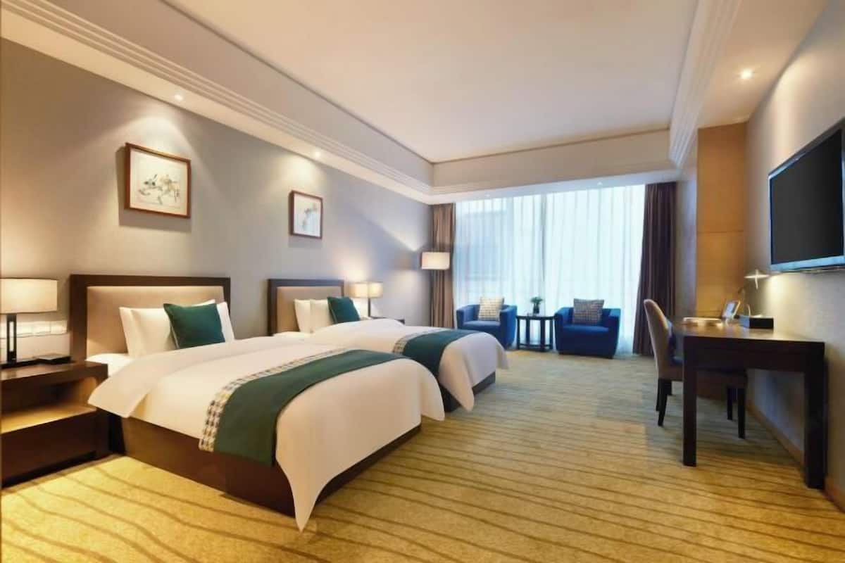 A hotel room with two beds, a desk, a chair, a TV, and a large window with curtains.