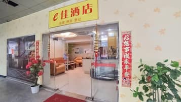 A hotel entrance with a sign, a reception area, and a red mat at the door.