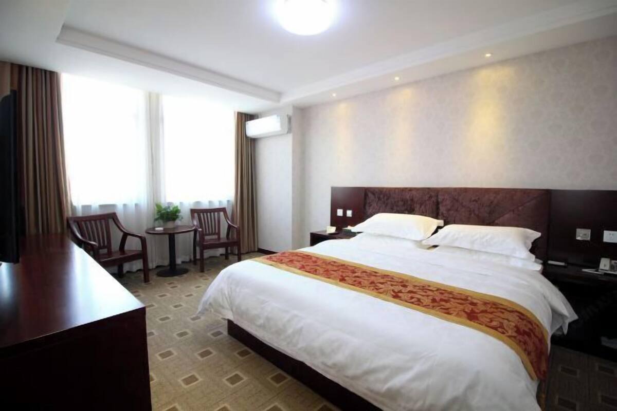 A hotel room with a large bed, a desk, two chairs, a small table, and a window with curtains.