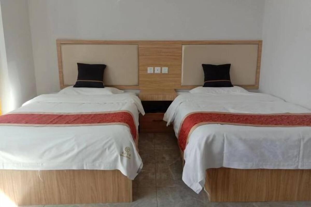 A hotel room with two beds, each with a wooden headboard, white bedding, and red accents.