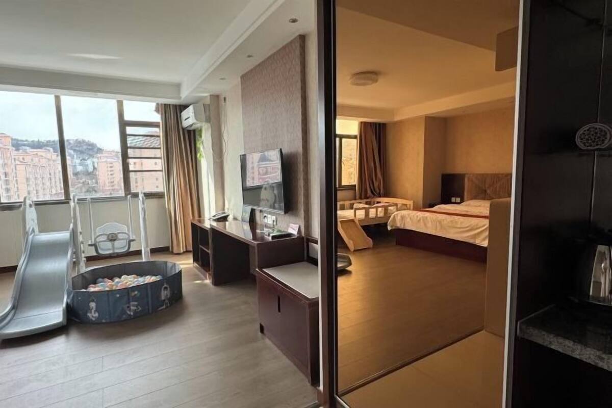 A hotel room with a bed, desk, chair, TV, and a view of buildings.