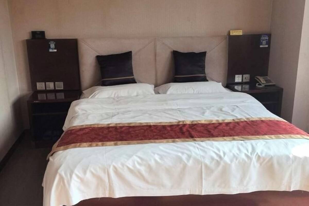 A hotel room with a bed, two bedside tables, and a wall-mounted telephone.
