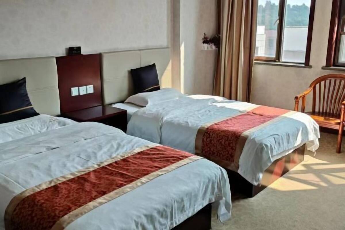 A hotel room with two beds, a nightstand, a chair, and a window with curtains.