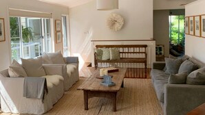 A spacious living room with a large window, a wooden bench, and a coffee table. - Omanu Shelly Beach (Port Macquarie)