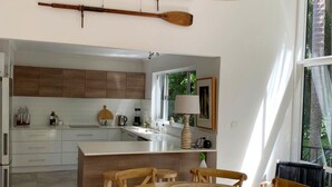A modern kitchen with wooden cabinets, a central island, and a dining area with wooden chairs. - Omanu Shelly Beach (Port Macquarie)