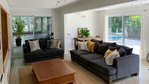 A spacious living room with a large grey sofa, a wooden coffee table, and a dining area with a table and chairs. - Omanu Shelly Beach (Port Macquarie)