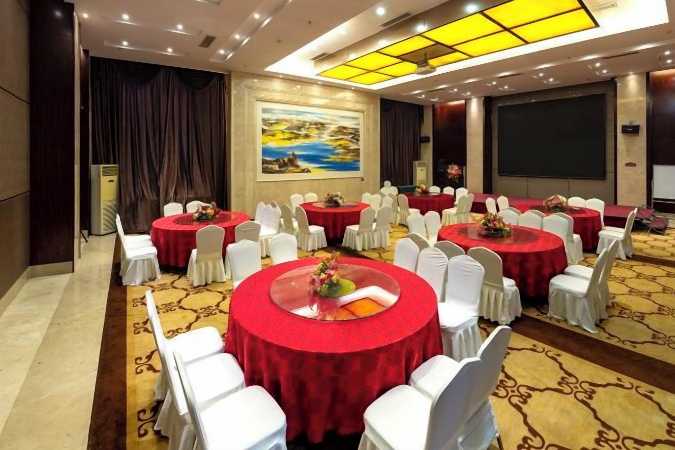 A conference room with multiple round tables, white chairs, and a carpeted floor.