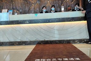 A reception desk with a marble back wall, a wooden floor mat, and a person standing to the right. - Kunming Southwest Hotel (Kunming)