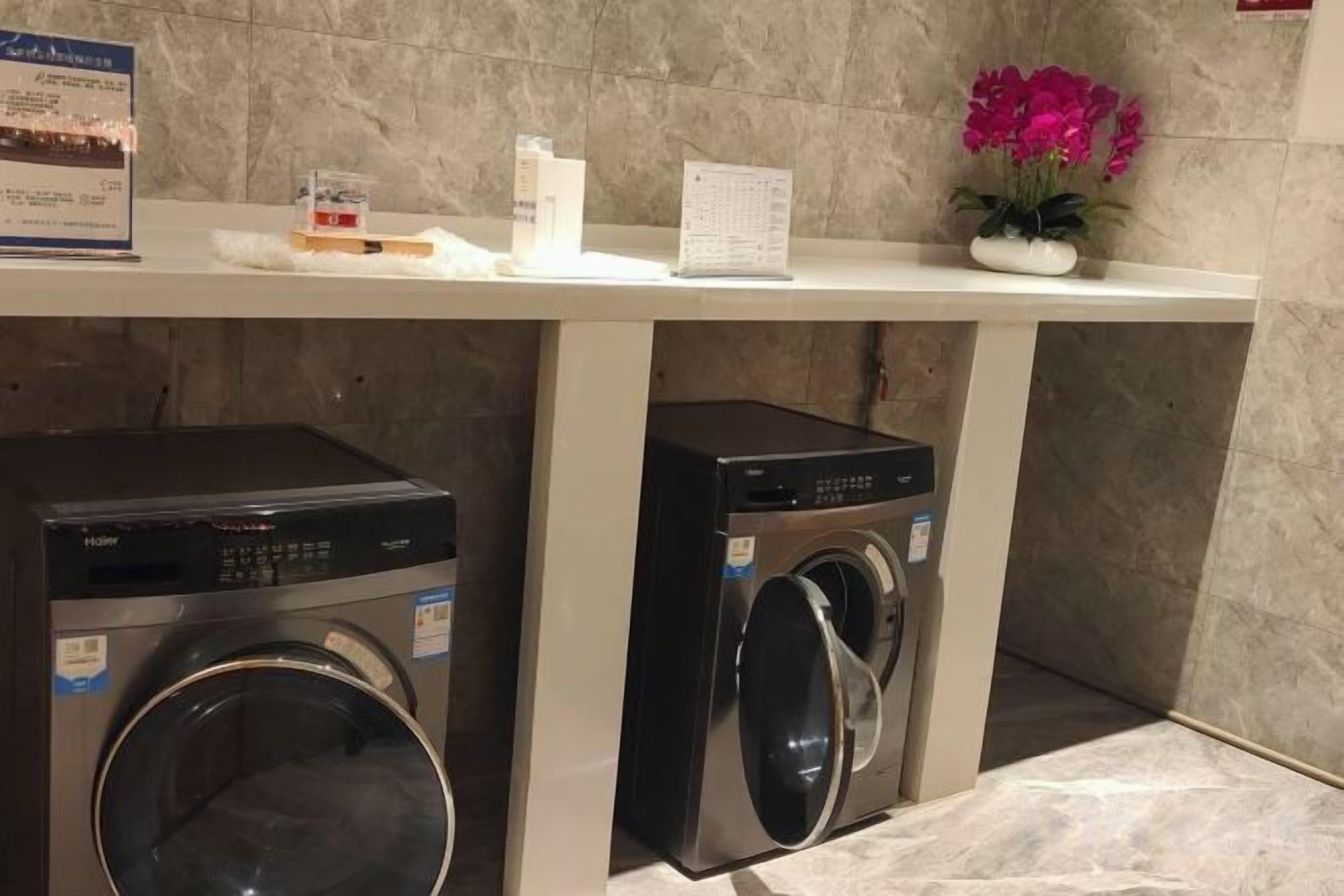 A laundry area with two front-loading washing machines under a white counter, a potted plant, and a small sign.