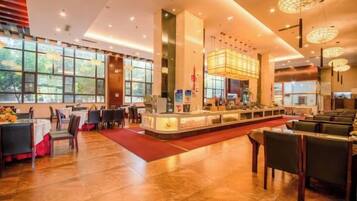 A spacious hotel lobby with a central bar area, multiple seating arrangements, and large windows providing natural light.