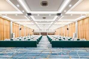 Une salle de conférence avec des rangées de chaises vertes, un sol recouvert de moquette et un plafond doté d’un éclairage encastré.