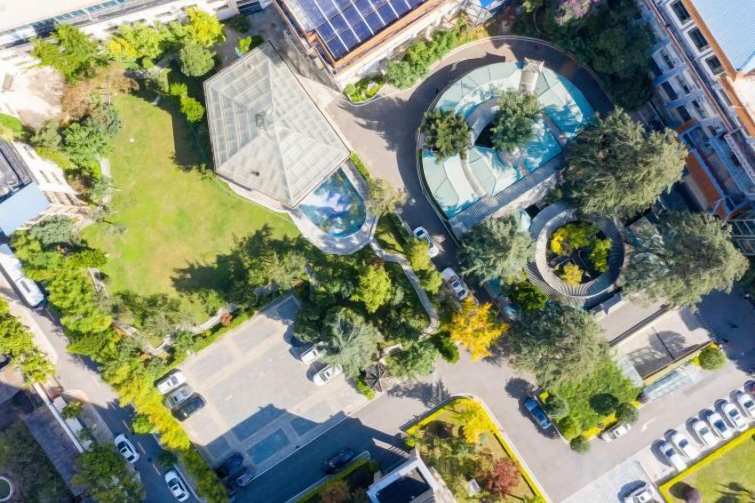 An aerial view of a residential area with a swimming pool, a curved building, and surrounding greenery.
