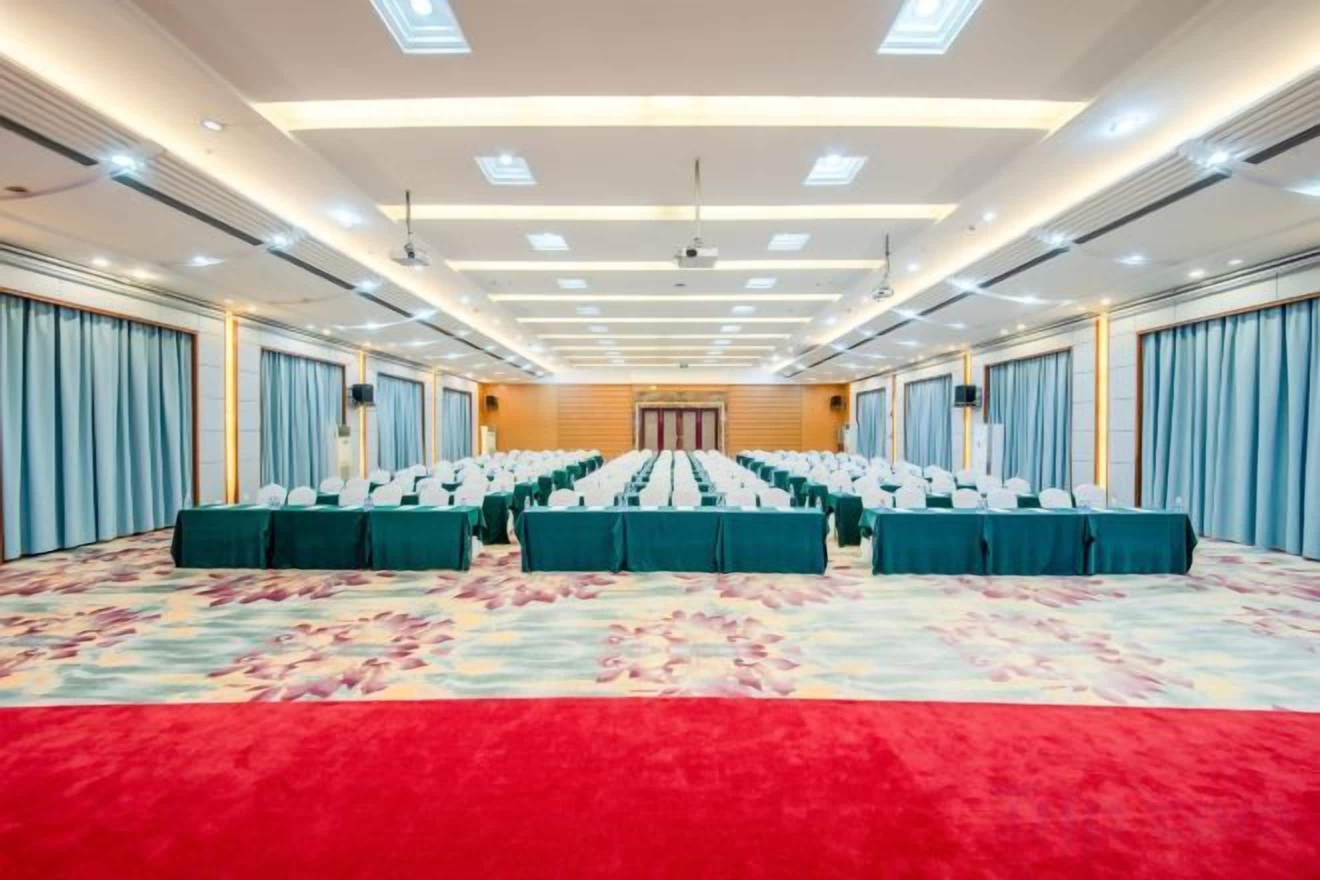 A conference room with rows of tables and chairs, a red carpet, and a patterned carpet.