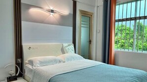 A neatly made bed with a white headboard, a bedside table with a lamp, and a window with curtains. - HaiBei Hostel (Shenzhen)