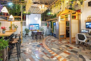 A restaurant with a checkered floor, wooden tables, chairs, hanging plants, and a TV screen. - HaiBei Hostel (Shenzhen)
