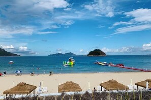 A beach with thatched umbrellas, a pier, and boats on the water. - HaiBei Hostel (Shenzhen)