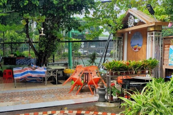 An outdoor seating area with tables and chairs, surrounded by greenery and a view of a body of water. - HaiBei Hostel (Shenzhen)