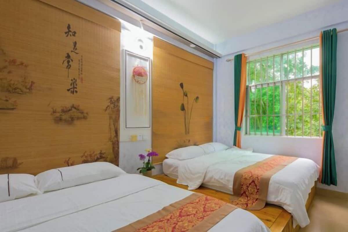A hotel room with two beds, a wooden headboard with calligraphy, a window with curtains, and a small vase with flowers.