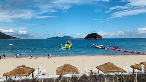 A beach with clear blue water, a pier, and thatched umbrellas. - HaiBei Hostel (Shenzhen)