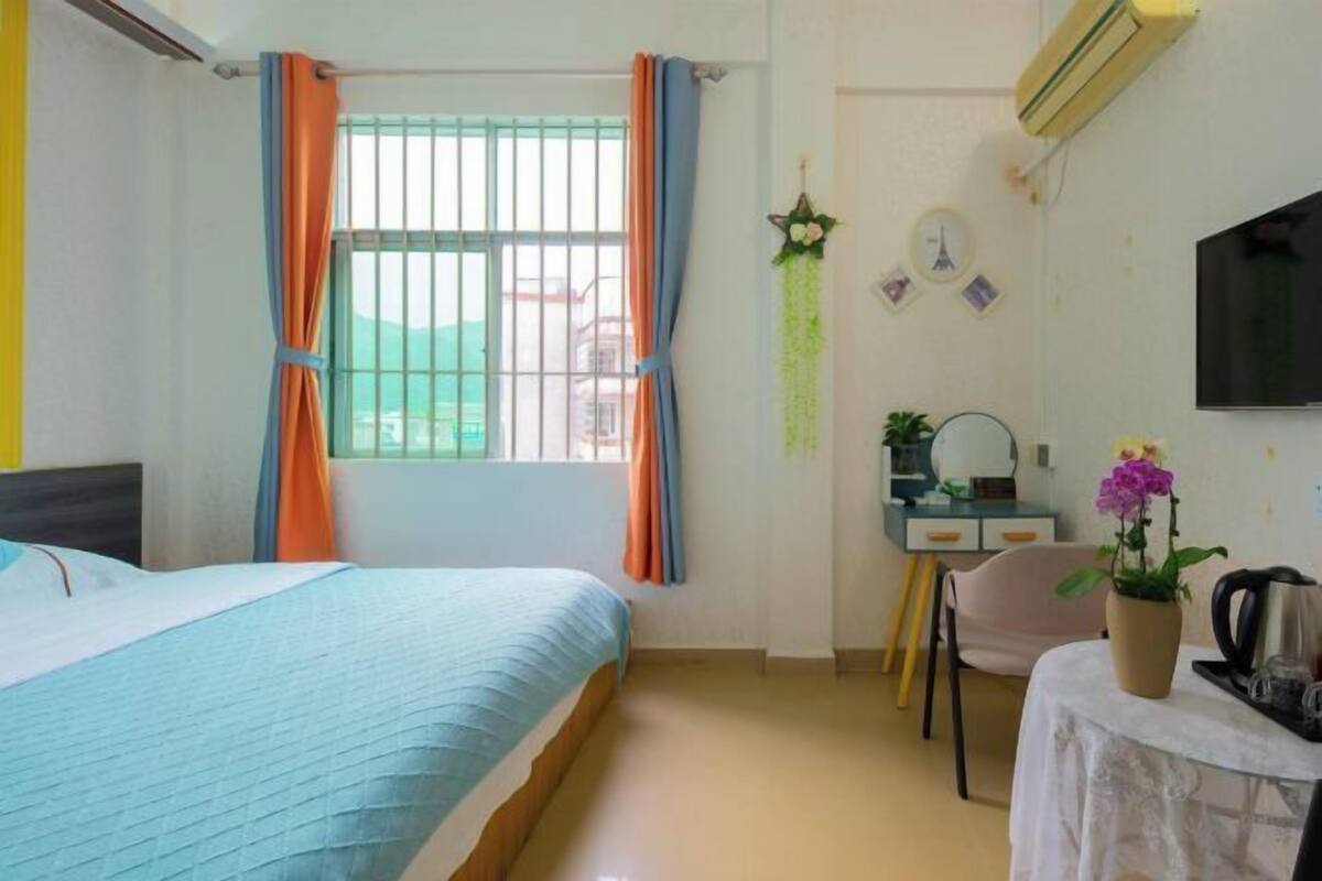 A hotel room with a bed, a desk with a chair, a television, and a window with curtains.