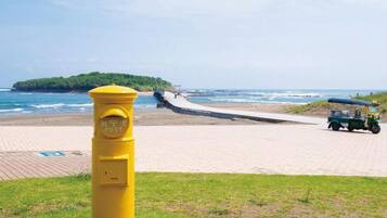 Una playa con un poste amarillo, un camino pavimentado y un vehículo a lo lejos.