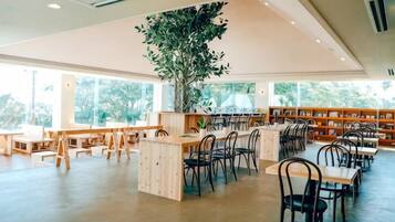 A spacious indoor area with tables and chairs, a large indoor plant, and bookshelves.