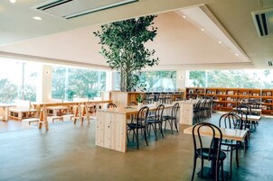 Un espacio interior amplio con mesas y sillas, una planta de gran tamaño y estanterías.