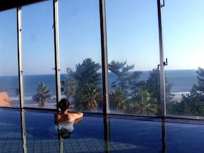 A person in a glass-enclosed infinity pool with a view of the ocean and palm trees. - Holiday Inn Resort MIYAZAKI by IHG (Miyazaki City)