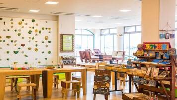 A children's play area with climbing walls, tables, chairs, and a bookshelf with toys.