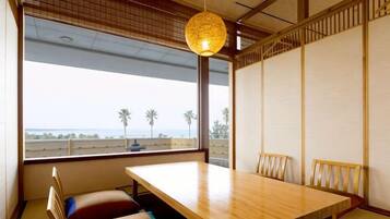 A traditional Japanese-style room with tatami flooring, a low wooden table, and a view of the sea through large windows.