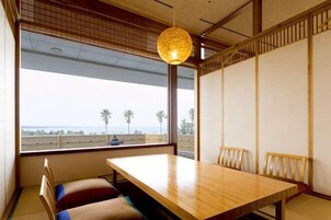 Una habitación tradicional japonesa con suelo de tatami, una mesa de madera baja y vistas al mar a través de amplios ventanales.