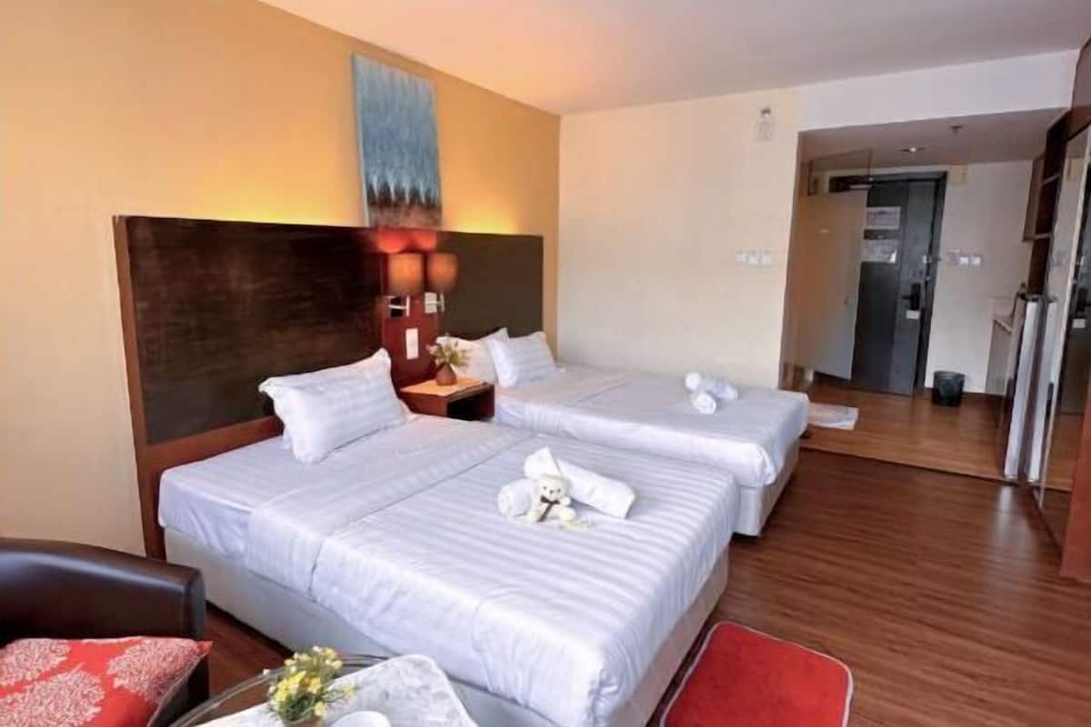 Hotellihuone, jossa on kaksi sänkyä, puulattia, taulu seinällä ja pieni pöytä, jonka päällä on maljakko täynnä kukkia.