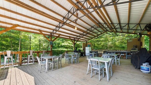 An outdoor covered patio with tables and chairs, a grill, and a refrigerator.