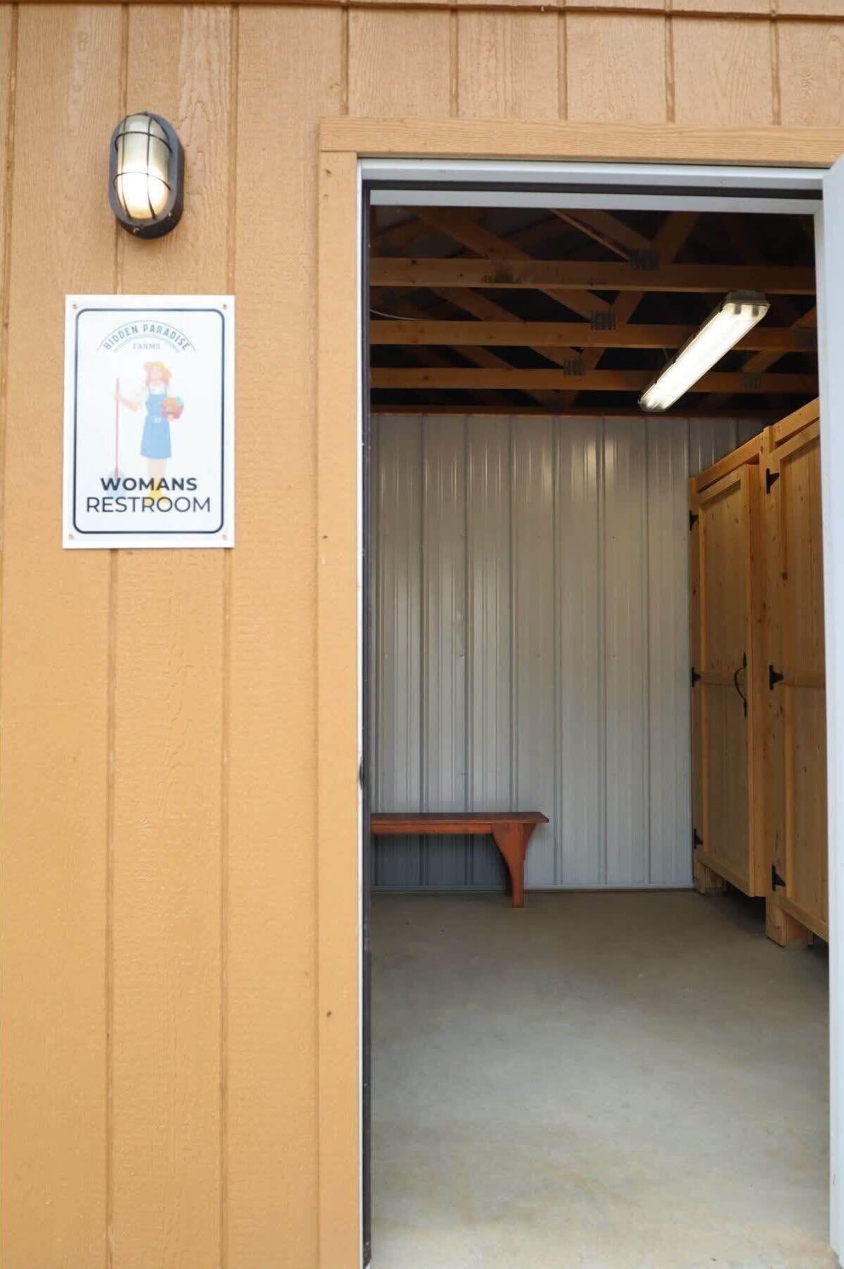 A women's restroom with a sign, a bench, and wooden doors.
