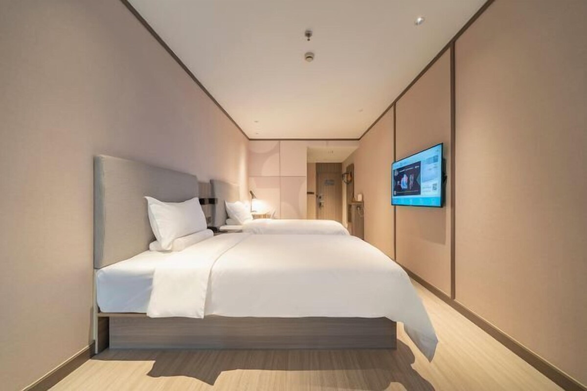 A modern hotel room with a large bed, a flat-screen TV mounted on the wall, and a wooden floor.
