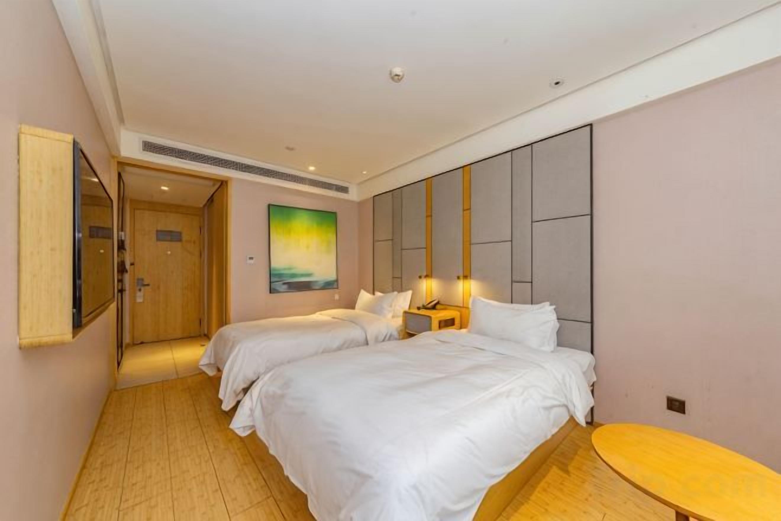 A hotel room with two beds, a small table, a painting on the wall, and a door leading to another room.