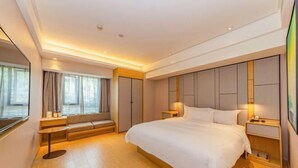 Ein modernes Hotelzimmer mit einem großen Bett, Nachttischen, einer Sitzecke und Blick auf die Stadt.