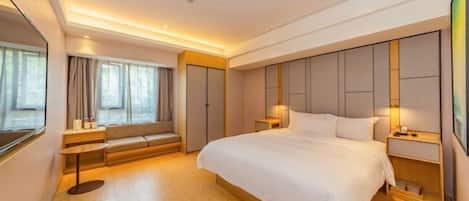 A modern hotel room with a large bed, bedside tables, a seating area, and a view of the city.