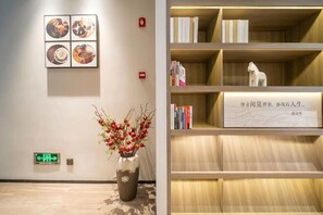 A reception area with a vase of flowers, a wall-mounted artwork, and a bookshelf with books and a decorative item. - HanTing Hotel (Shanghai Daning Music Plaza Xindian) (Shanghai)