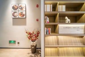 A reception area with a vase of flowers, a wall-mounted artwork, and a bookshelf with books and a decorative item. - HanTing Hotel (Shanghai Daning Music Plaza Xindian) (Shanghai)