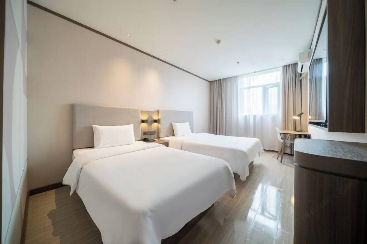 A hotel room with two beds, a desk, a chair, and a large window.