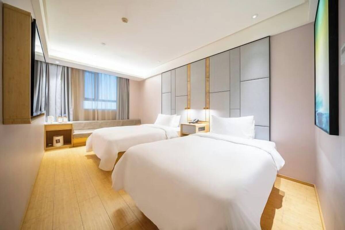 A hotel room with two beds, a large mirror, a TV, and a window with curtains.