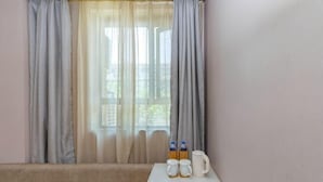 Ein Zimmer mit einer Couch, einem kleinen Tisch mit Krug und Flaschen sowie einem Fenster mit durchsichtigen Vorhängen.