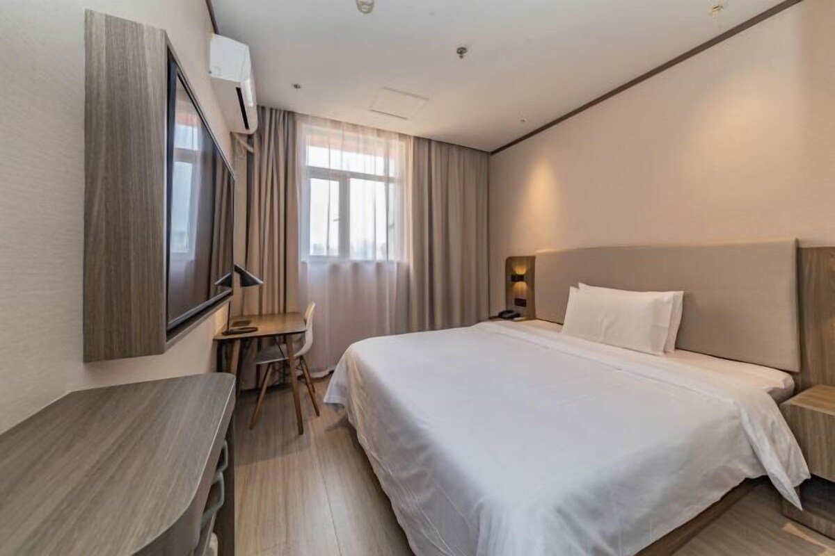 A hotel room with a bed, a desk, a chair, a TV, and a window with curtains.